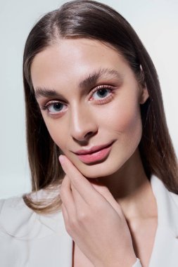 Genç bir kadın zarif bir gülümseme ile cazibesini sergiliyor, şık bir kıyafet ve sıcak bir ışık giyiyor..