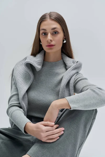 Sade gri elbiseli genç bir kadın zarif bir ifade sergiliyor..