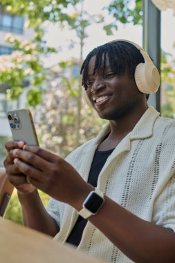 Yakışıklı bir genç adam telefonuna bakarken kulaklıkla müzik dinlerken gülümser..