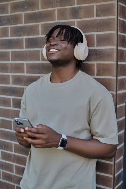 Kulaklıklı yakışıklı genç adam duvarın karşısında duruyor, mesajlaşırken gülümsüyor..