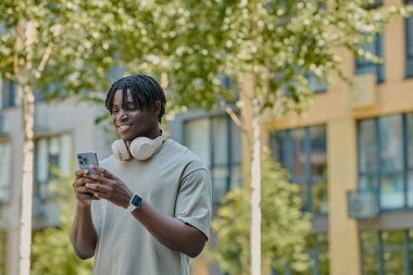 Genç adam canlı bir şehir bölgesinde yürürken telefonuna bakarken gülümsüyor..