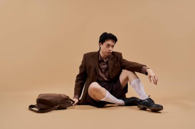 Kahverengi bir ceketin içinde zarif pozlar veren genç bir Asyalı stüdyoda sofistike bir stil yayıyor..