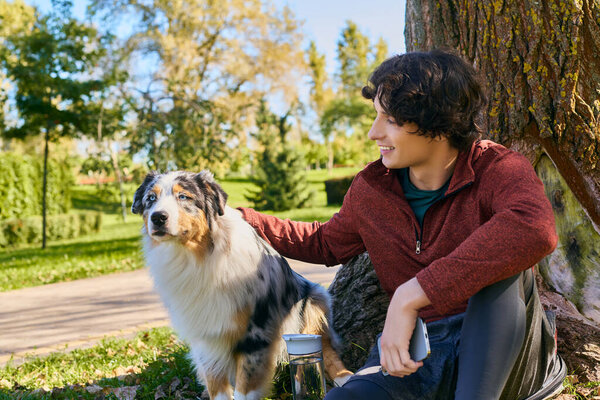 A young man in a spring jacket happily walks with his beloved Australian Shepherd dog.