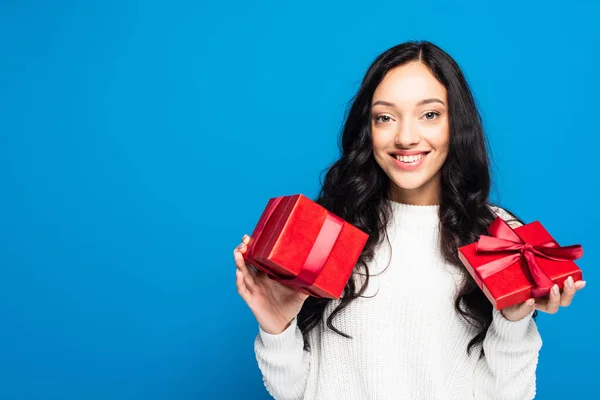 Young happy woman in sweater holding christmas present isolated on blue — Stock Photo