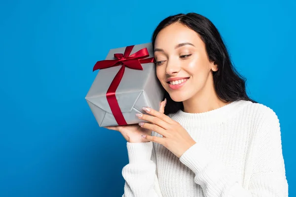 Joyful woman in knitted sweater holding gift box isolated on blue — Stock Photo