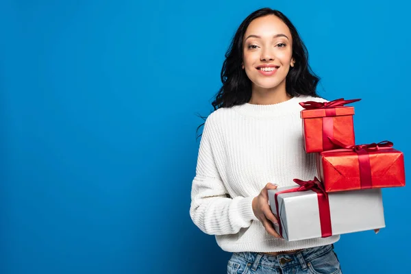 Щаслива жінка в трикотажному светрі тримає подарункові коробки ізольовані на синьому — стокове фото