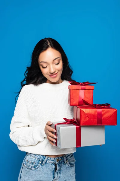 Щаслива молода жінка в трикотажному светрі тримає подарункові коробки ізольовані на синьому — стокове фото