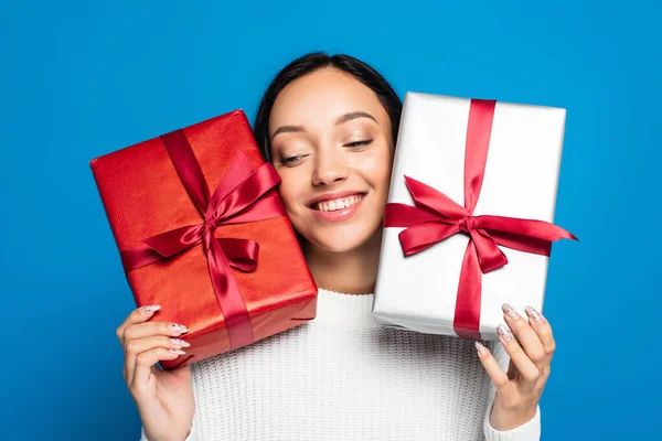 Pleased young woman in knitted sweater holding gift boxes isolated on blue — Stock Photo