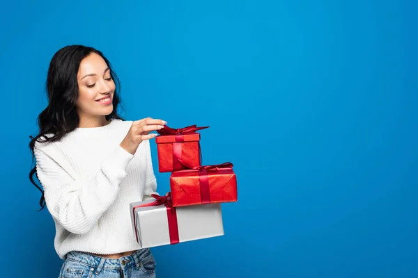 Alegre joven mujer en punto suéter celebración de cajas de regalo aislado en azul - foto de stock