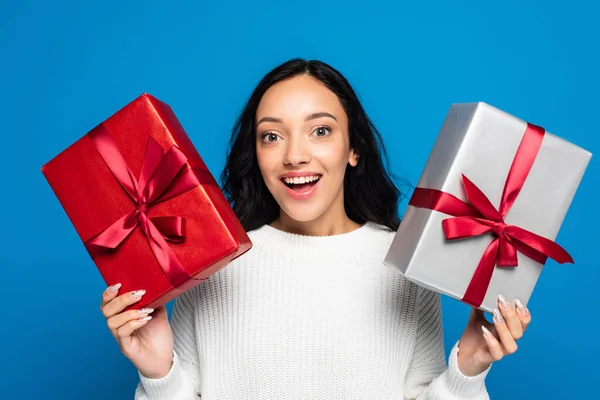 Excitée jeune femme en pull tricoté tenant des boîtes-cadeaux isolées sur bleu — Photo de stock