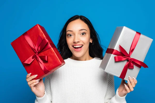 Eccitata giovane donna in maglia maglione contenente scatole regalo isolato su blu — Foto stock