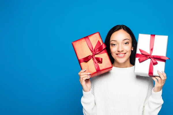 Cheerful woman in knitted sweater holding gifts isolated on blue — Stock Photo