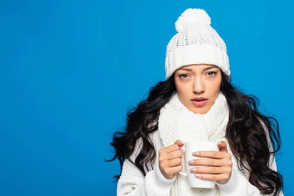 Jeune femme en bonnet tricoté et écharpe tenant tasse tout en gelant isolé sur blanc — Photo de stock