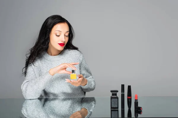 Brünette Frau mit roten Lippen hält Flasche mit Parfüm isoliert auf grau — Stockfoto