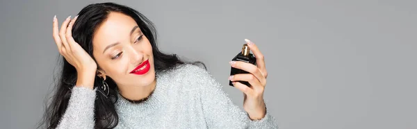Mujer complacida con labios rojos sosteniendo botella con perfume aislado en gris, bandera — Stock Photo