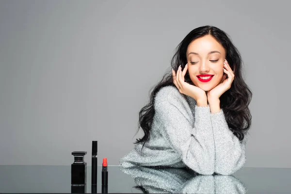 Femme heureuse avec des lèvres rouges regardant le flacon avec du parfum et des cosmétiques décoratifs isolés sur gris — Photo de stock