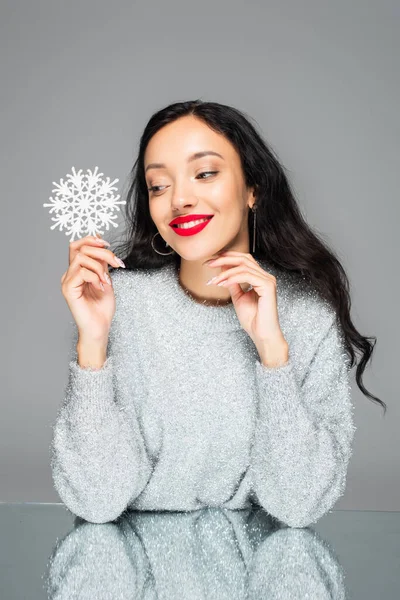 Mujer complacida con labios rojos sosteniendo copo de nieve decorativo aislado en gris - foto de stock