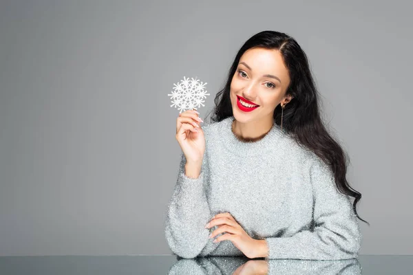 Erfreut junge Frau mit roten Lippen hält dekorative Schneeflocke isoliert auf grau — Stockfoto