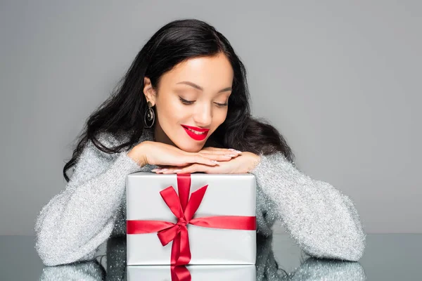 Mujer feliz con labios rojos mirando caja de regalo aislado en gris - foto de stock