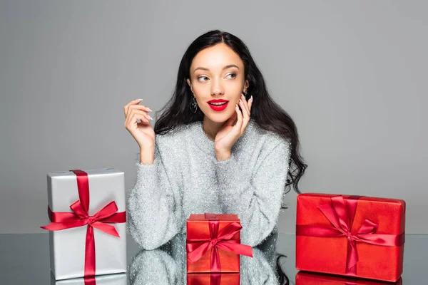 Femme heureuse avec des lèvres rouges regardant loin près des boîtes-cadeaux isolées sur gris — Photo de stock