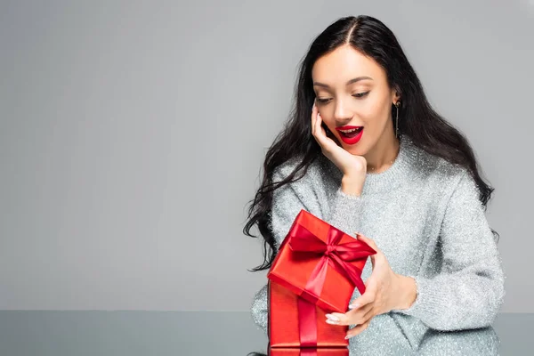 Surprised woman with red lips looking at present isolated on grey — Stock Photo