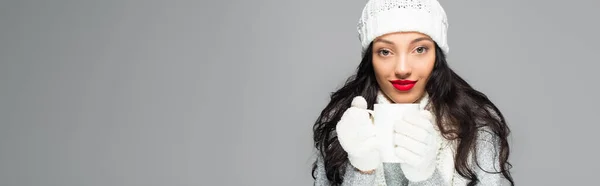 Joyful and brunette woman in winter outfit holding cup isolated on grey, banner — Stock Photo