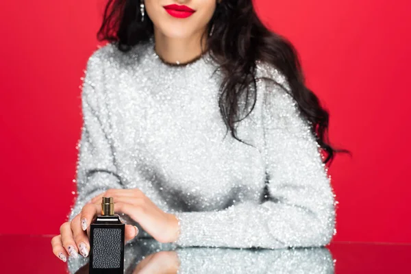 Cropped view of brunette woman holding bottle with perfume isolated on red — Stock Photo