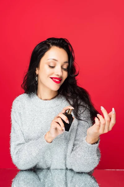 Frau hält Flasche in der Hand und sprüht Parfüm auf Rot — Stockfoto