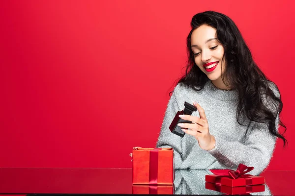 Pleased woman holding bottle with perfume near gift box isolated on red — Stock Photo