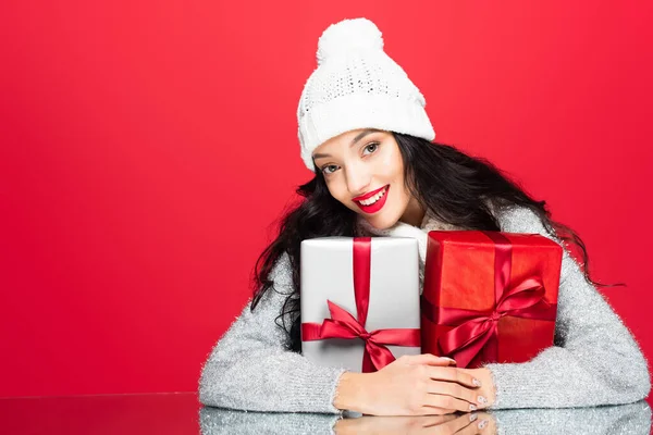 Joyful woman in hat embracing christmas presents isolated on red — Stock Photo