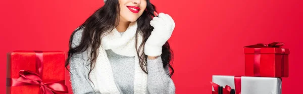 Vue recadrée de joyeuse femme tenant rouge à lèvres près de cadeaux de Noël isolé sur rouge, bannière — Photo de stock