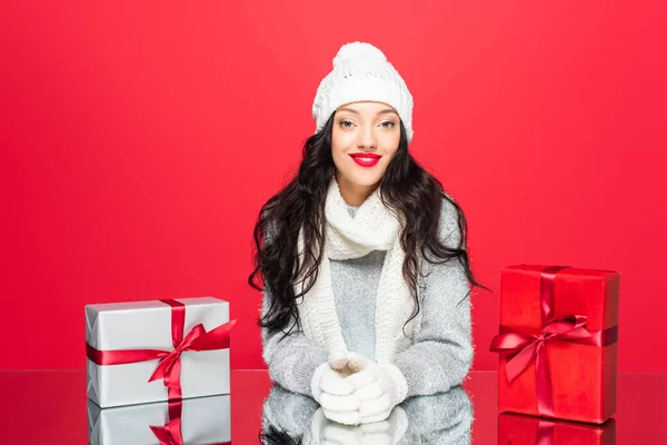 Femme joyeuse en tenue d'hiver souriant près de Noël présente isolé sur rouge — Photo de stock