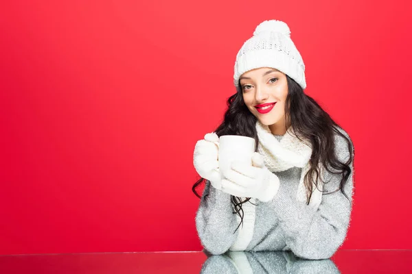 Glückliche Frau im winterlichen Outfit mit Becher und Getränk auf rotem Grund — Stockfoto