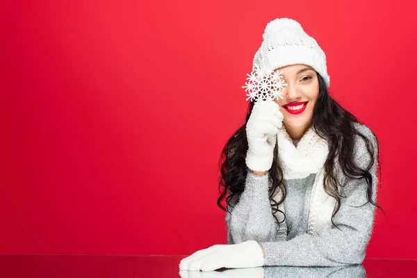 Mujer feliz en traje de invierno sosteniendo copo de nieve decorativo aislado en rojo - foto de stock