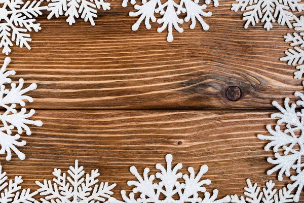 Colocación plana con copos de nieve decorativos sobre fondo de madera marrón, concepto de año nuevo - foto de stock