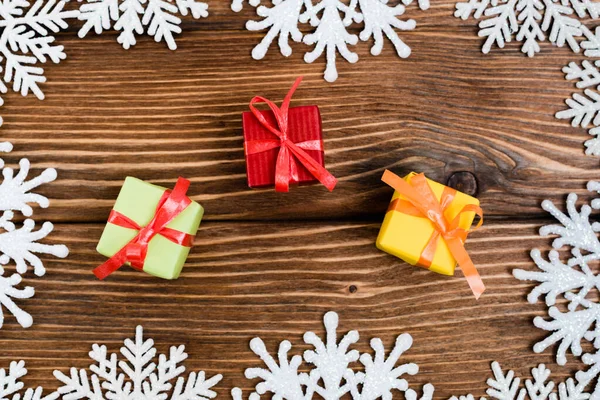Вид зверху на маленькі подарункові коробки біля декоративних сніжинок на дерев'яному фоні, концепція нового року — стокове фото