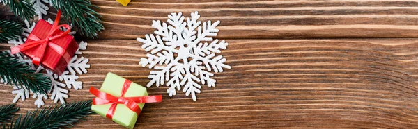 Вид сверху на декоративные снежинки, маленькие подарочные коробки и сосновую ветвь на деревянном фоне, баннер — стоковое фото