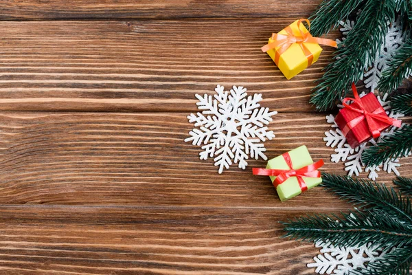 Вид зверху на декоративні сніжинки, маленькі подарункові коробки та гілки сосни на дерев'яному фоні, концепція нового року — стокове фото