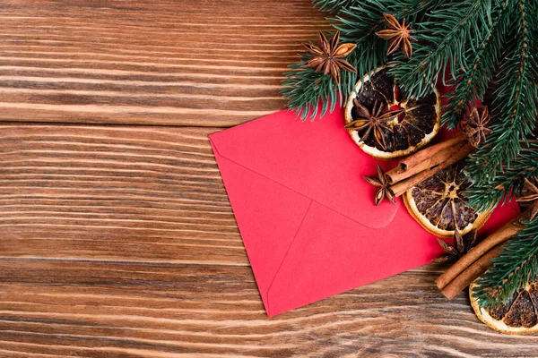 Top view of red envelope near anise stars, cinnamon sticks, dry orange slices and pine branches on brown wooden background — Stock Photo