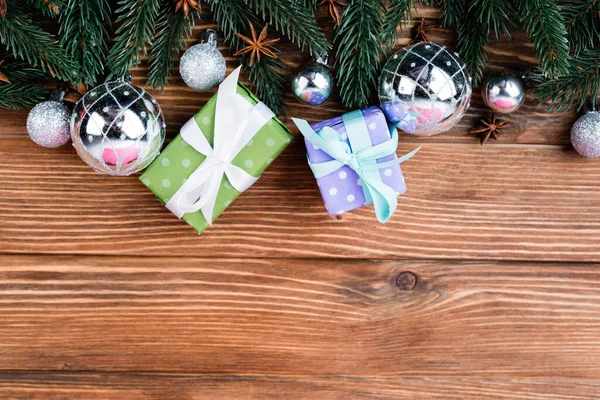 Draufsicht auf kleine Geschenkschachteln, Kugeln, Anissterne und Tannenzweige auf braunem Holzhintergrund — Stockfoto