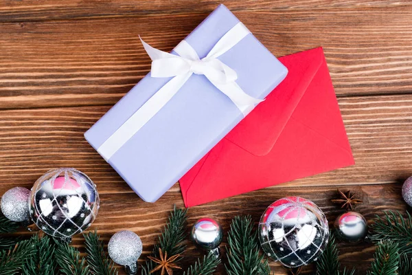 Top view of mini gift box with envelope near pine branches, baubles and anise stars on brown wooden background — Stock Photo