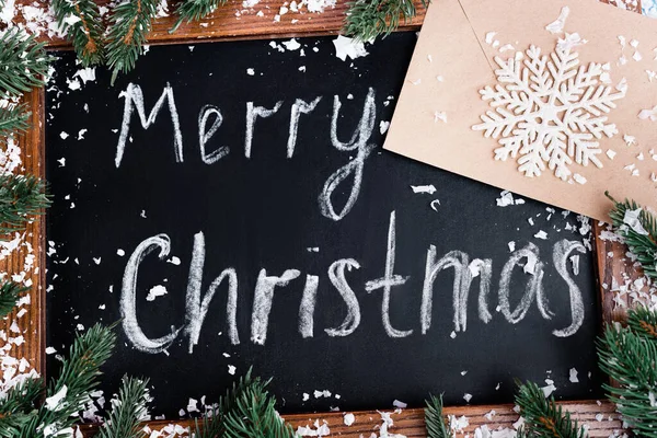 Vista superior de pizarra con letras navideñas alegres, ramas de pino, sobre y copo de nieve decorativo - foto de stock
