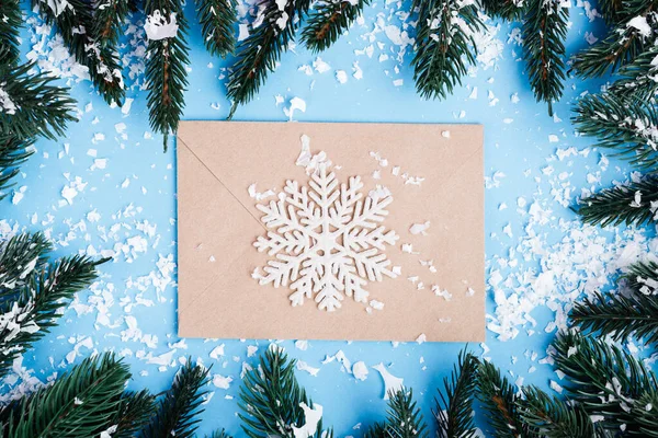 Draufsicht auf Briefumschlag, dekorative Schneeflocke und Tannenzweige mit Kunstschnee auf blauem Hintergrund — Stockfoto