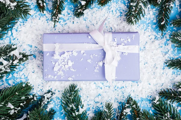 Vue du dessus du petit coffret cadeau près des branches de pin et de la neige artificielle sur fond bleu — Photo de stock