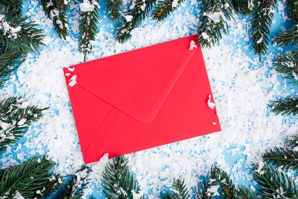 Top view of red envelope, artificial snow and pine branches on blue background, new year concept — Stock Photo