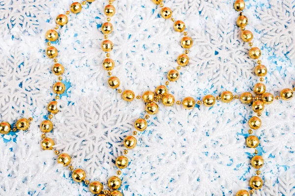 Vista de cerca de las cuentas de oro con copos de nieve decorativos y nieve artificial sobre fondo azul, concepto de año nuevo - foto de stock