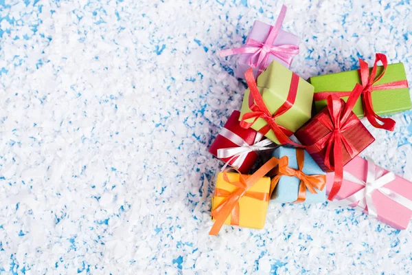 Vista superior de pequeños regalos con nieve artificial sobre fondo azul, concepto de año nuevo - foto de stock