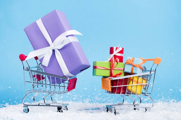 Nivel de superficie de los carritos de la compra con pequeños regalos sobre fondo azul, concepto de año nuevo - foto de stock