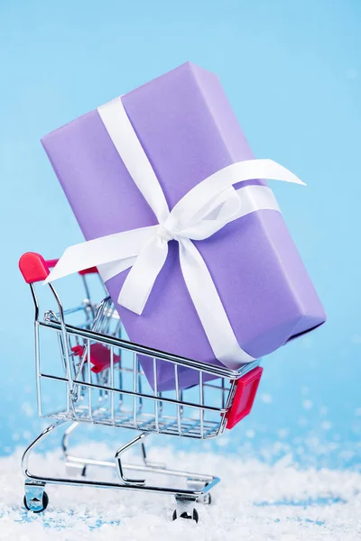 Close up view of little gift in shopping trolley on blue background, new year concept — Stock Photo