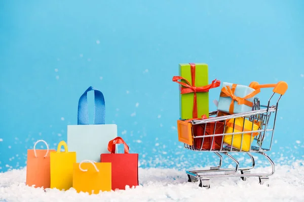 Tiny paper bags near trolley with bunch of little gifts on blue background, new year concept — Stock Photo